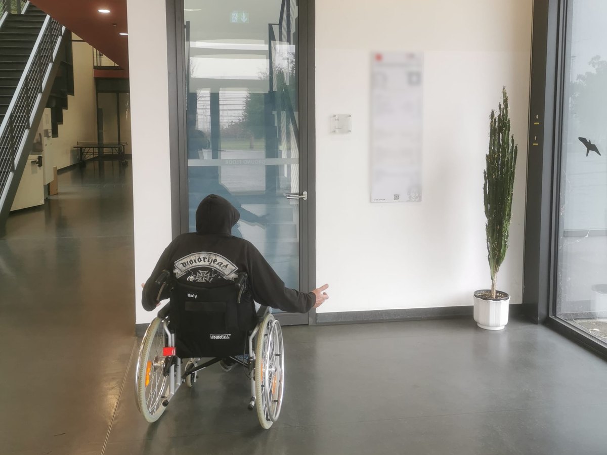Rollstuhlfahrer vor einer geschlossenen Glastür ohne Antrieb